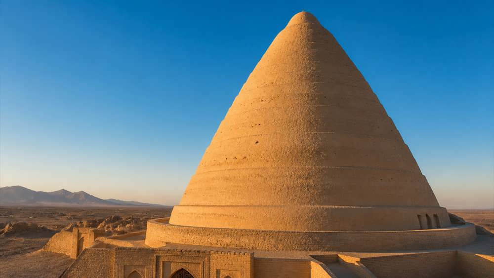 عکسی واقع گرایانه و باشکوه از یک یخدان خشتی باستانی ایرانی در دل کویر تحت تابش نور خورشید.