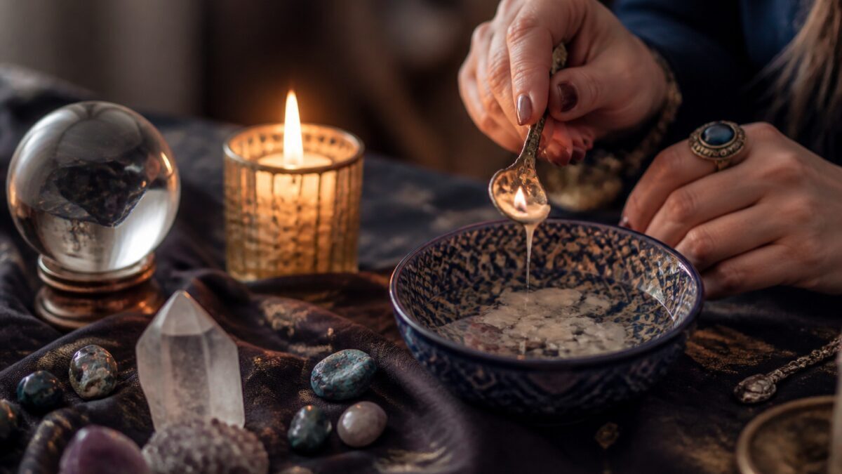 شمع روشن کنار کاغذ یادداشت و فنجان چای روی میز چوبی در نور طبیعی