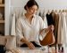 کیف چرمی خنثی، ساعت، گوشواره و گردنبند مینیمال کنار لباس‌های کپسولی تاخورده