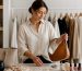 کیف چرمی خنثی، ساعت، گوشواره و گردنبند مینیمال کنار لباس‌های کپسولی تاخورده