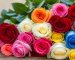 دسته‌ای از رزهای قرمز، زرد، سفید، صورتی و آبی روی میز چوبی در نور طبیعی
