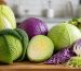 سر کلم سبز تازه روی تخته چوبی کنار برگ‌های جداشده در آشپزخانه روشن