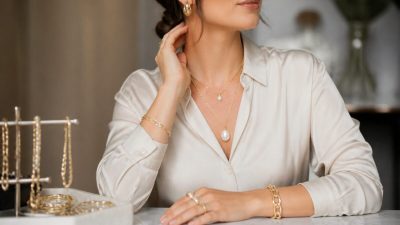 نمای نزدیک از زنی با گوشواره‌های طلایی ظریف و گردنبند لایه‌ای مینیمال در نور طبیعی
