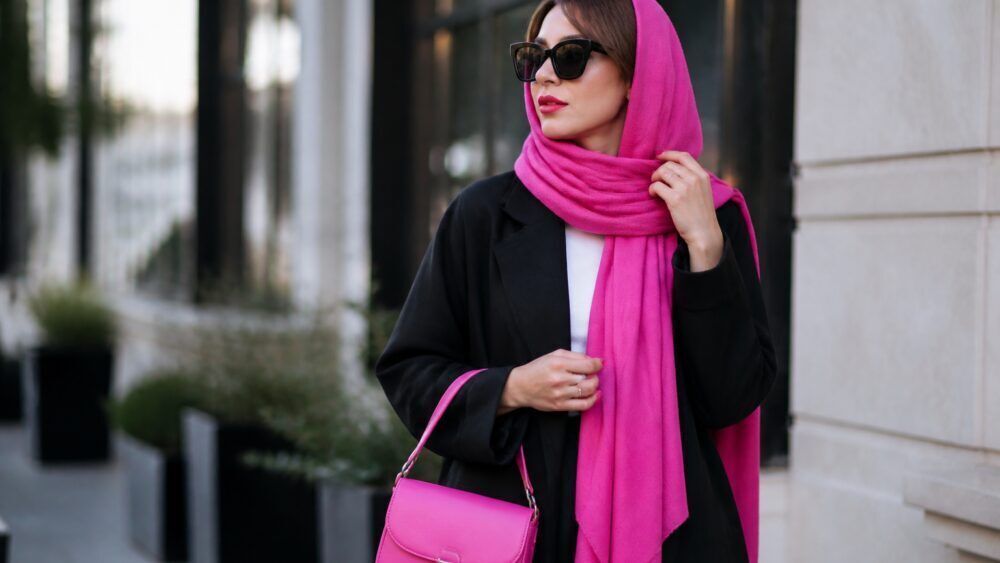 زنی در خیابان شهری با مانتوی خنثی و کیف دستی صورتی هات پینک