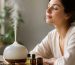 دیفیوزر سرامیکی در حال پخش بخار کنار شیشه اسانس اسطوخودوس و حوله سفید روی میز چوبی