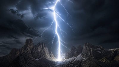 عکسی سینمایی از برخورد قدرتمند یک صاعقه به زمین در یک منظره کوهستانی تاریک و طوفانی.