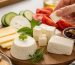 بشقاب چوبی با پنج نوع پنیر کم‌نمک، انگور تازه و سبزی‌های معطر روی میز روشن