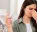 زنی با حالت ناراحتی بینی و چشم‌ها را کنار شیشه عطر روی میز آرایشی می‌پوشاند