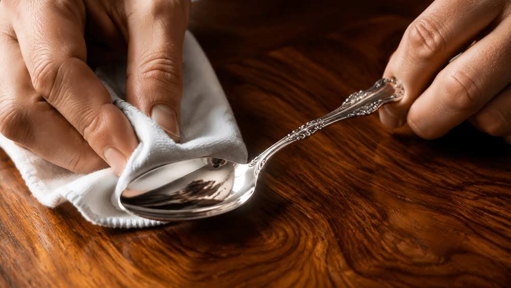 تمیز کردن و خشک کردن ظروف نقره با یک پارچه نرم روی میز چوبی براق.