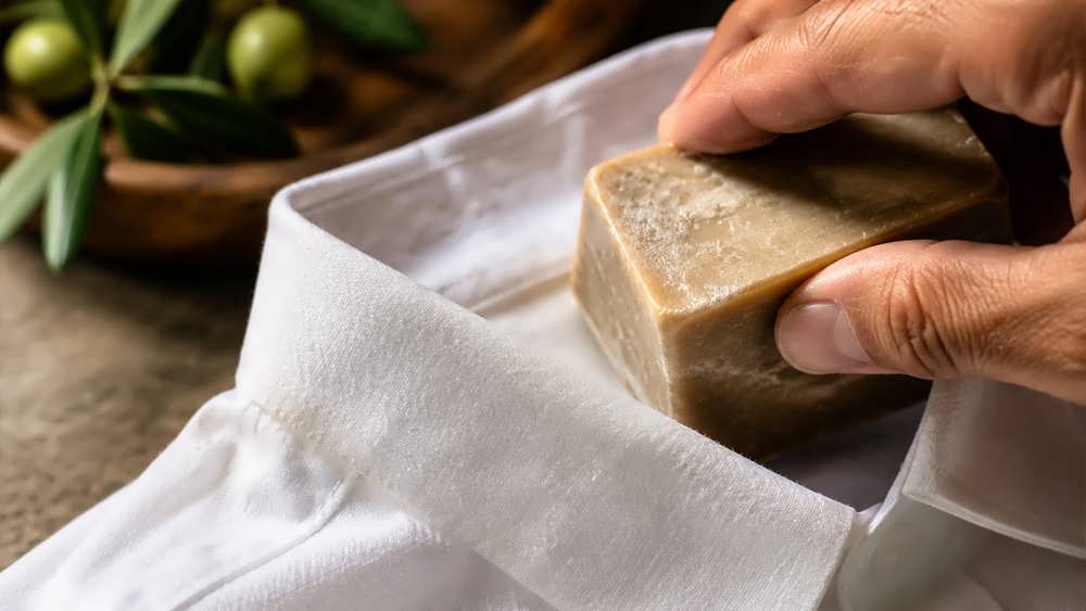 مالیدن ملایم صابون سنتی و طبیعی روی یقه یک پیراهن مردانه نخی سفید برای پیش درمان لکه چربی.