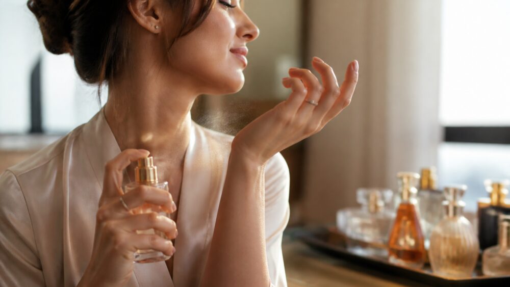 زنی در حال اسپری کردن عطر روی نبض مچ دست، بدون مالیدن مچ ها به هم