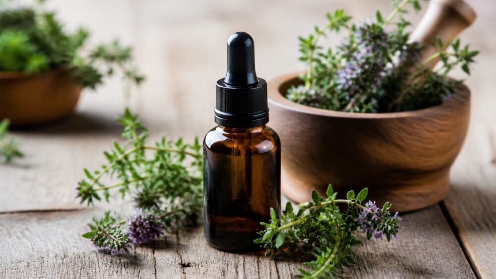 بطری شیشه ای تینکچر آویشن با قطره چکان کنار برچسب دستور مصرف و چند شاخه آویشن