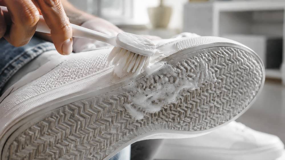 تمیز کردن لبه های یک کفش کتانی سفید با استفاده از مسواک و خمیردندان.