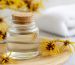 بطری شیشه‌ای عصاره گیاهی در کنار شاخه‌های گل زرد ویچ هازل روی میز روشن