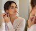 زنی در حال تنظیم گوشواره‌های آویز کریستالی اشکی در مقابل آینه