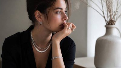 زنی با استایل کلاسیک مشکی و گردنبندهای نقره لایه‌ای و انگشترهای متعدد