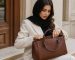 مجموعه‌ای از کیف‌های دستی چرمی زنانه شامل مدل بزرگ، کراس‌بادی رنگی و کیف کوچک روی میز چوبی