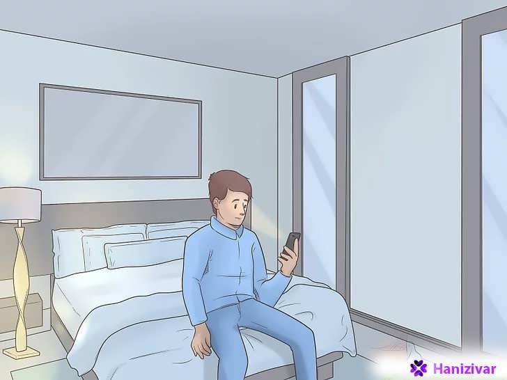 مردی نشسته روی لبه تخت در حال نگاه کردن به گوشی موبایل
