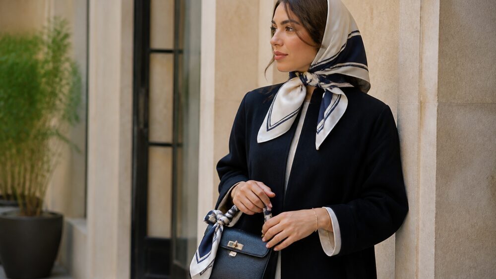 زنی با مانتوی مشکی و روسری ابریشمی رنگی، همراه کیف دستی هماهنگ در فضای شهری